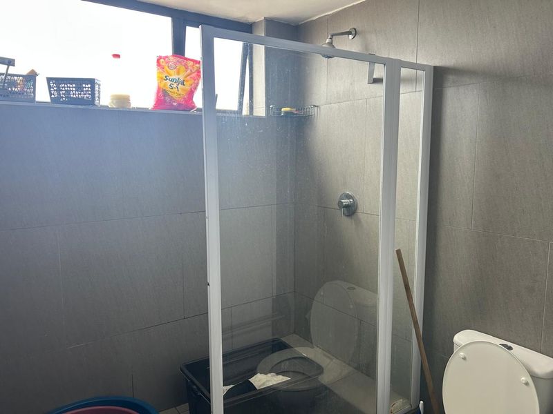 A functional bathroom featuring a glass-enclosed shower, wall-mounted shower head, and a standard toilet with grey wall tiling.