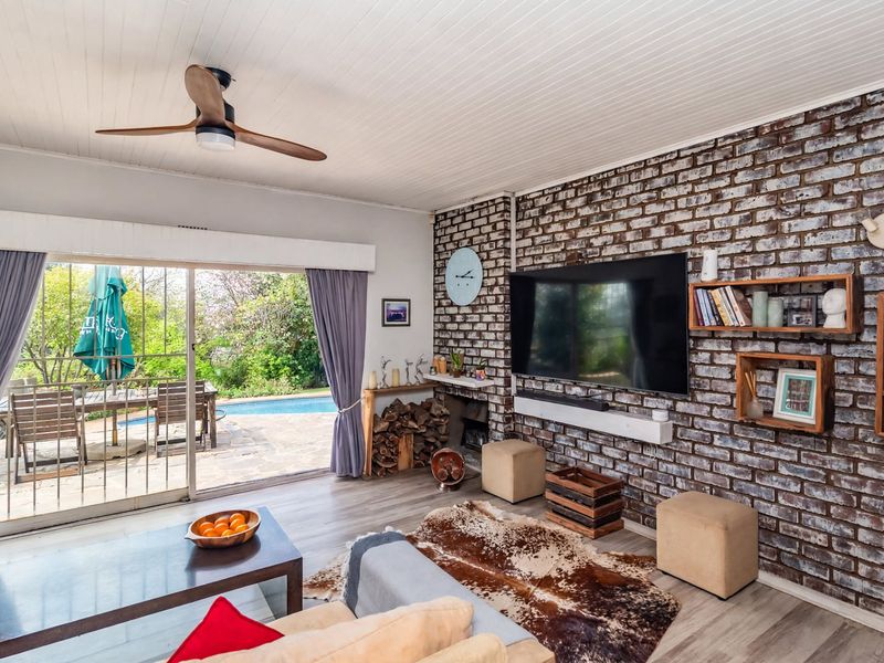Spacious living room featuring an exposed brick feature wall, ceiling fan, and large sliding glass doors providing direct access to the outdoor pool area.