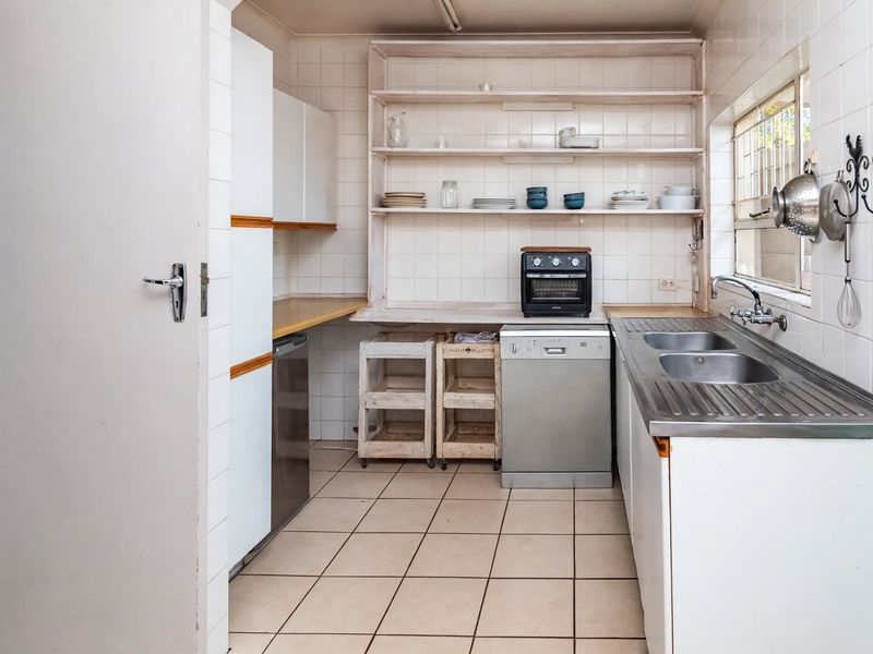 A functional kitchen featuring tiled walls and flooring, open shelving, and a double stainless steel sink with integrated cabinetry.
