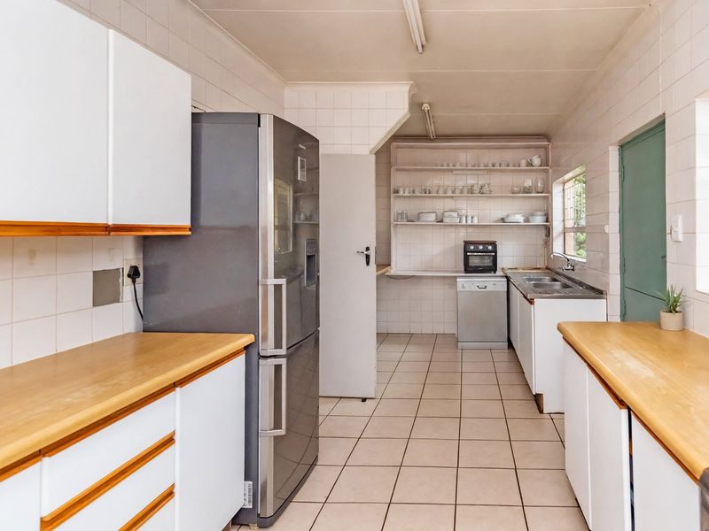 A functional kitchen featuring white cabinetry, laminate countertops, tiled walls, and open shelving, offering a practical layout with ample storage space.