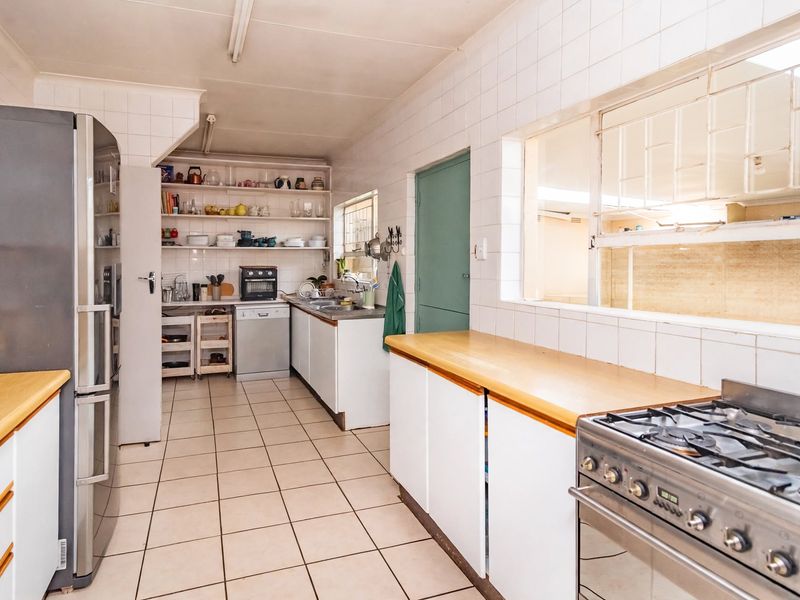 Functional kitchen featuring tiled walls and flooring, wooden countertops, gas stove, and ample built-in cabinetry with open shelving for storage.