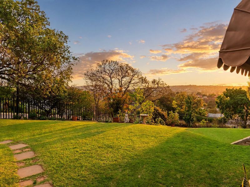 A well-maintained garden featuring a lush lawn, stone pathway, and metal perimeter fencing, offering scenic sunset views.