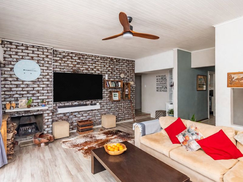 A cozy living room featuring an exposed brick wall, a built-in fireplace, and a modern ceiling fan, creating a warm and inviting atmosphere.