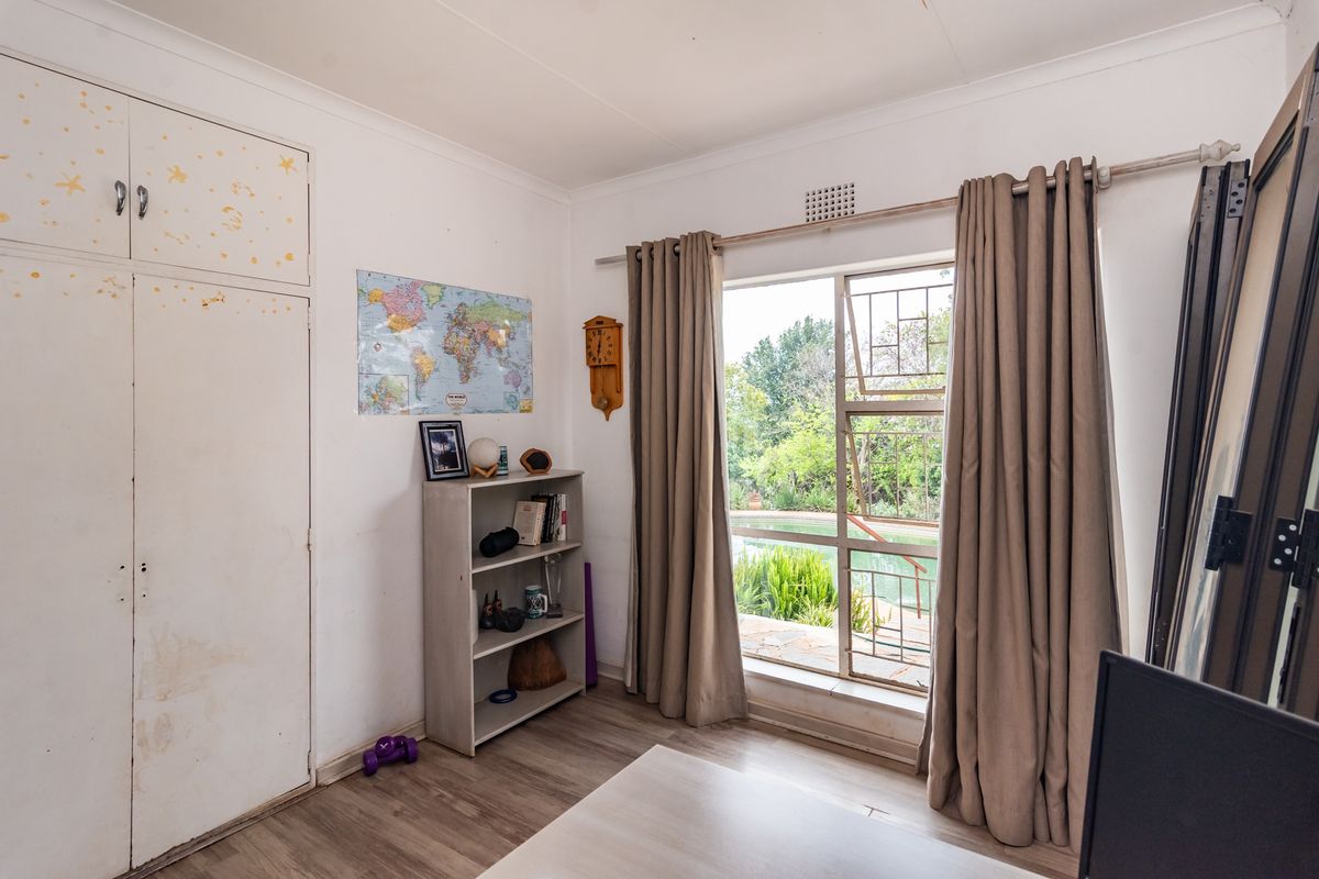 A bedroom featuring built-in cupboards, laminate flooring, and a window with security gate overlooking the garden.