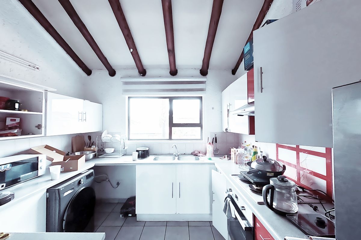 A functional kitchen featuring exposed timber ceiling beams, white cabinetry, tiled flooring, and a double bowl sink with integrated oven and extractor fan.