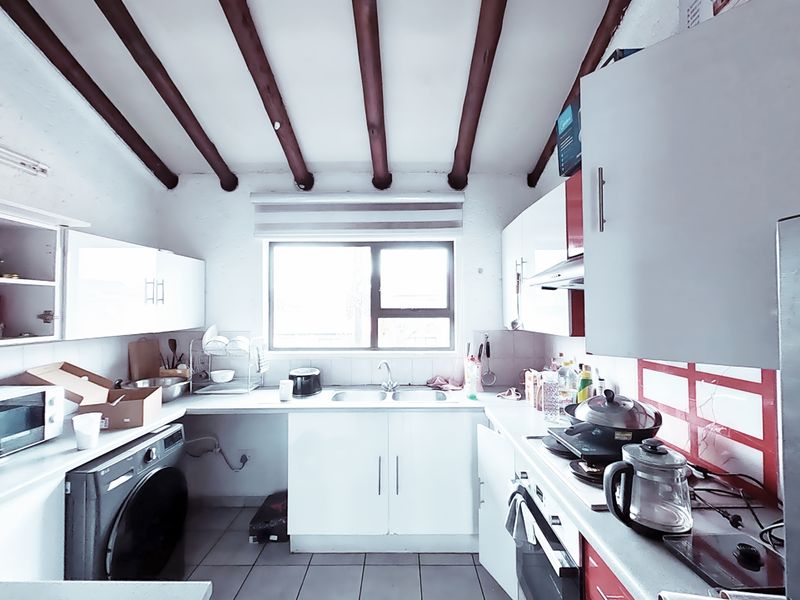 A functional kitchen featuring exposed timber ceiling beams, white cabinetry, tiled flooring, and a double bowl sink with integrated oven and extractor fan.
