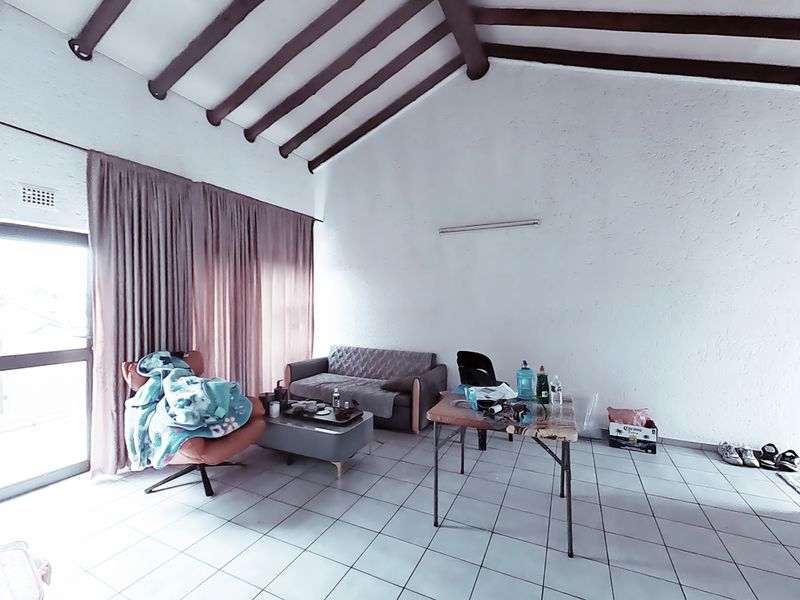 Living area featuring high vaulted ceilings with exposed timber beams, tiled flooring, and access to an outdoor area through a sliding glass door.