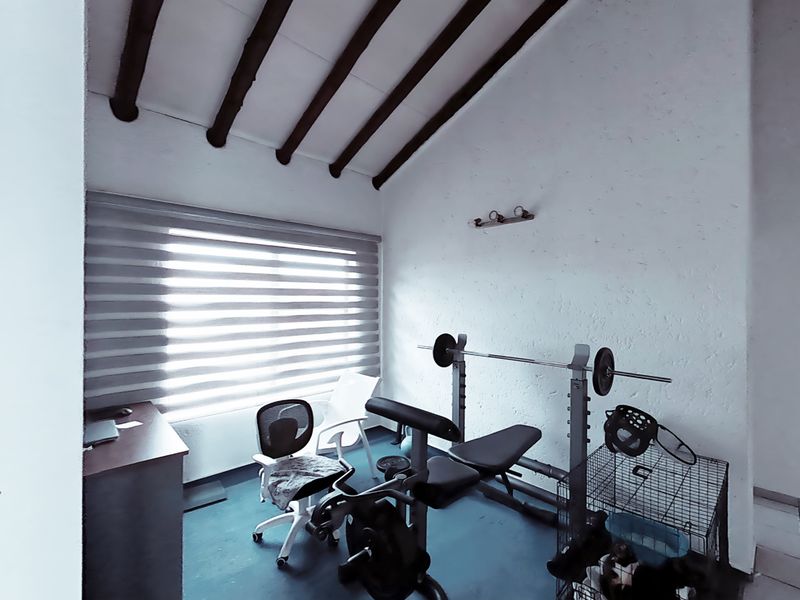 A functional gym space featuring exposed timber ceiling beams and natural light through roller blinds, suitable for a home workout area.