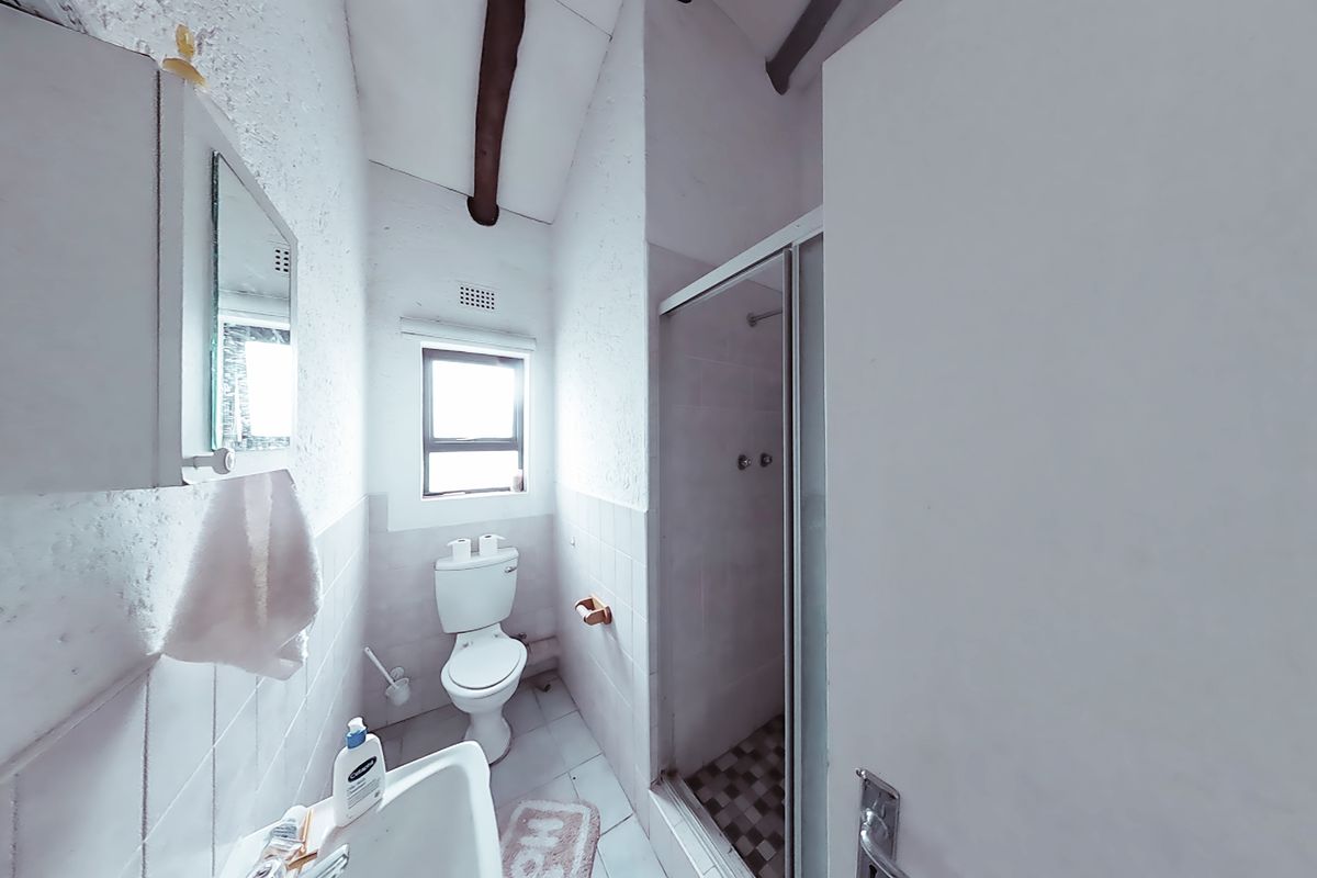 A compact bathroom featuring a shower enclosure, toilet, and wall-mounted basin, characterized by a dated aesthetic and exposed ceiling beam.