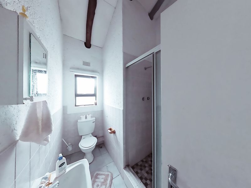 A compact bathroom featuring a shower enclosure, toilet, and wall-mounted basin, characterized by a dated aesthetic and exposed ceiling beam.