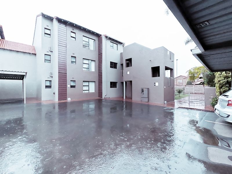 Exterior view of a multi-story townhouse complex featuring a paved parking area and covered carports.