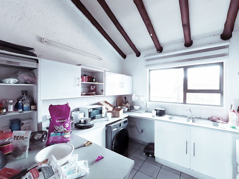 A functional kitchen featuring exposed timber ceiling beams, white cabinetry, a double basin sink, and tiled flooring with an integrated washing machine.
