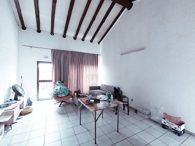 Living room featuring high vaulted ceilings with exposed timber beams, tiled flooring, and access to an outdoor area through a glass sliding door.
