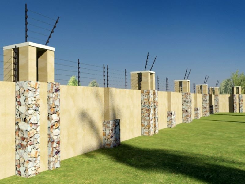 A secure perimeter wall featuring stone-clad masonry pillars and integrated electric fencing, bordering a well-maintained lawn area.