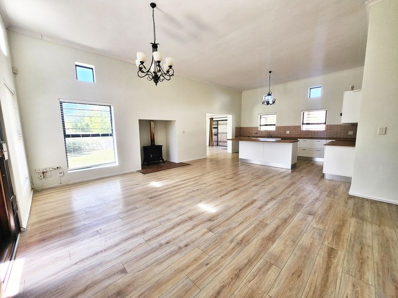 Spacious open-plan living and kitchen area featuring light wood-look laminate flooring, a wood-burning fireplace, and a functional kitchen island with built-in cabinetry.