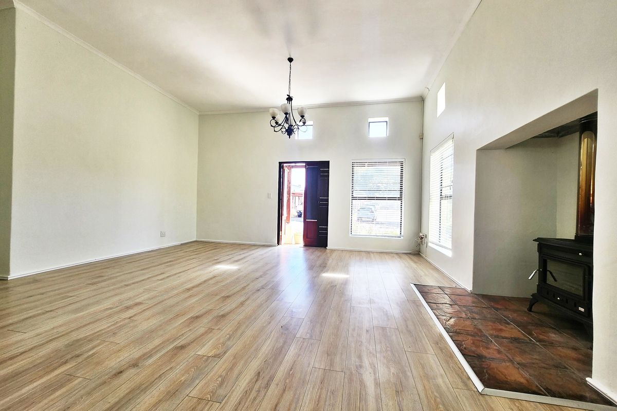 Spacious, light-filled living room featuring modern laminate flooring, a built-in fireplace with a tiled hearth, and neutral walls.