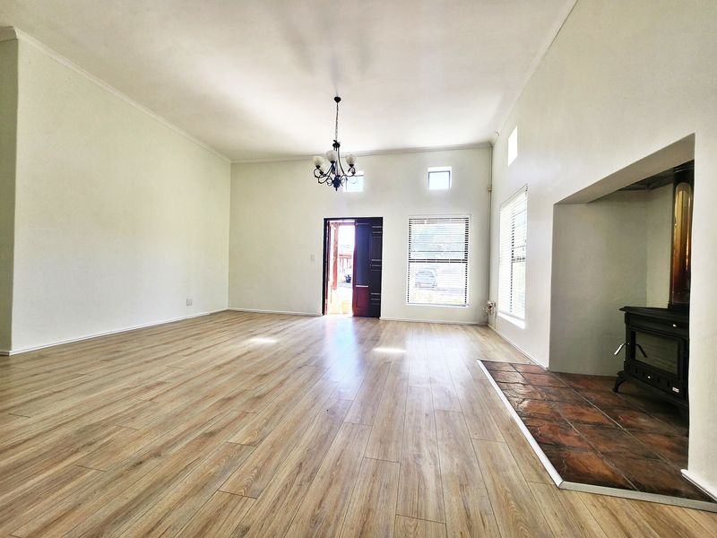 Spacious, light-filled living room featuring modern laminate flooring, a built-in fireplace with a tiled hearth, and neutral walls.