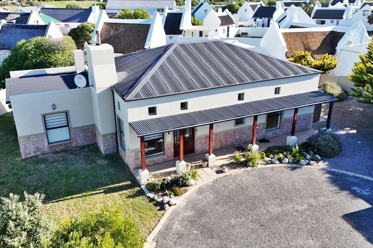 Aerial view of a well-maintained house featuring a corrugated metal roof, stone cladding, and a covered veranda with timber posts.