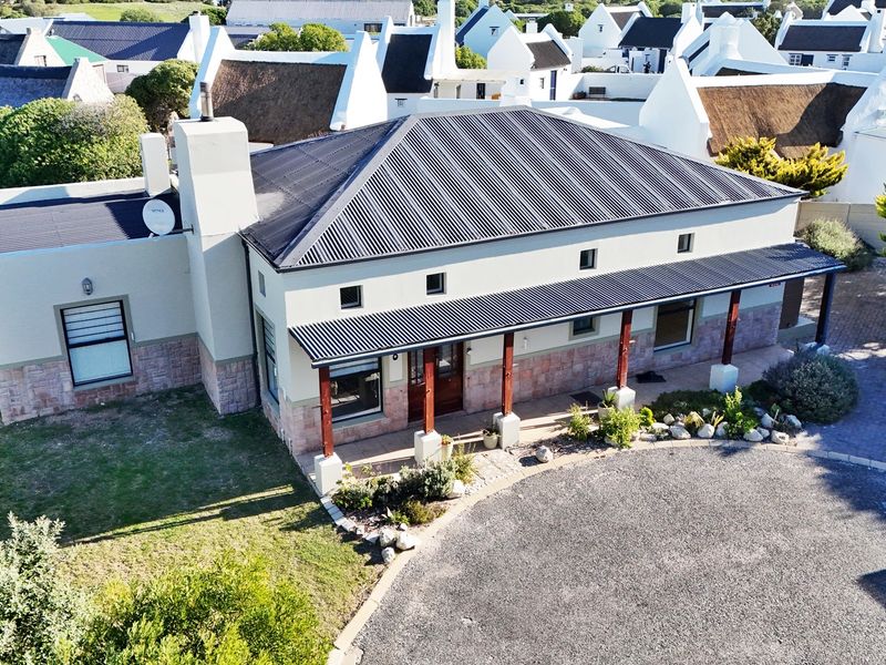 Aerial view of a well-maintained house featuring a corrugated metal roof, stone cladding, and a covered veranda with timber posts.