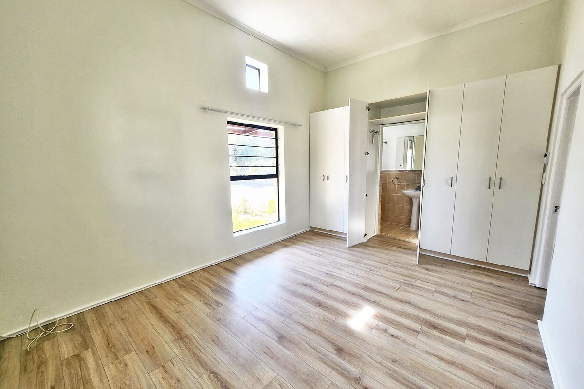 Spacious bedroom featuring light wood-look laminate flooring, built-in cupboards, and an en-suite bathroom, offering a clean and neutral canvas.