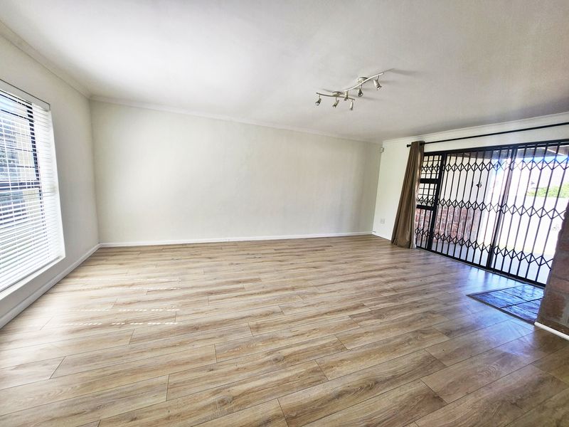 Spacious, empty living room featuring light wood-look laminate flooring, modern track lighting, and a secure sliding door leading to the exterior.