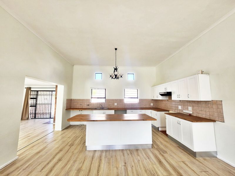 Spacious kitchen featuring a central island, white cabinetry, wooden countertops, tiled backsplash, and light-toned laminate flooring.
