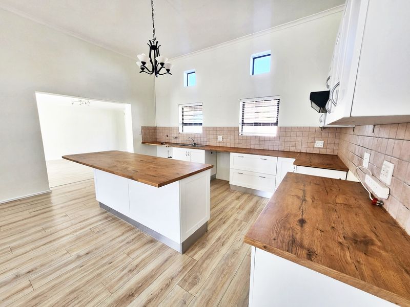 Spacious kitchen featuring a central island, wooden countertops, tiled backsplash, and ample built-in cabinetry with modern laminate flooring.