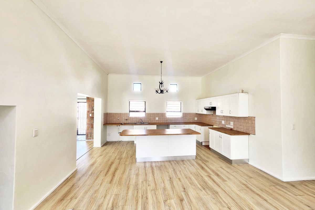Spacious open-plan kitchen featuring white cabinetry, wooden countertops, a central island, and light wood-look laminate flooring.