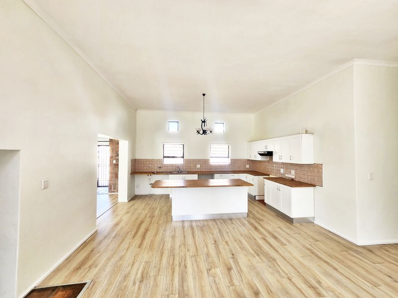 Spacious open-plan kitchen featuring white cabinetry, wooden countertops, a central island, and light wood-look laminate flooring.