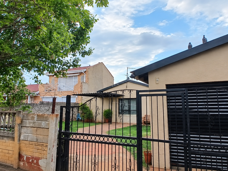 Front view of the property featuring a secure wrought iron gate, brick boundary wall with balustrade detailing, and a garage with a roller door.