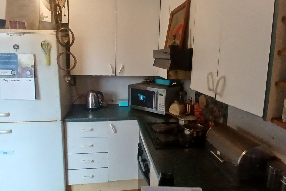 A compact kitchen featuring dated white cabinetry, laminate countertops, and integrated cooking appliances, offering potential for a modern renovation.