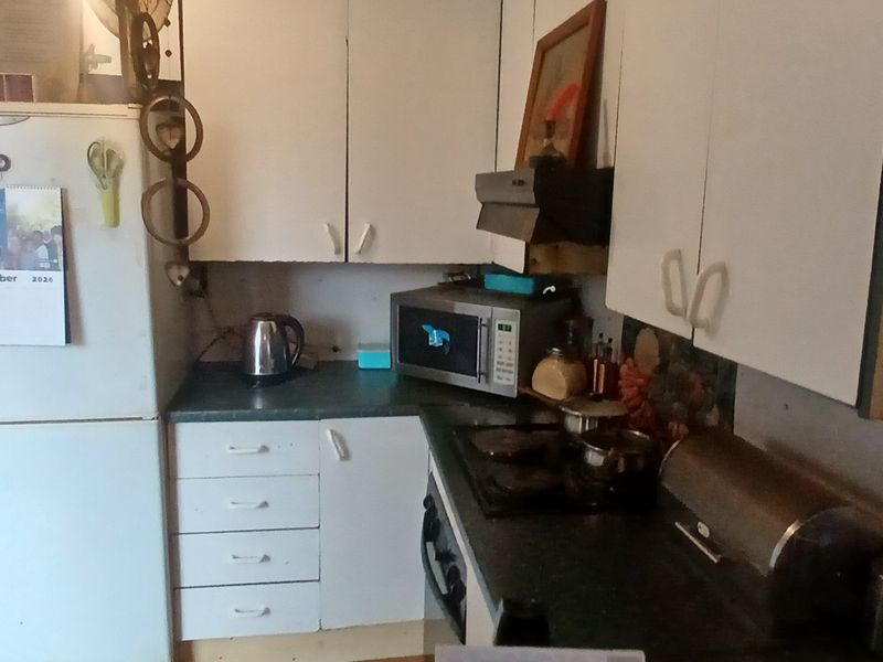 A compact kitchen featuring dated white cabinetry, laminate countertops, and integrated cooking appliances, offering potential for a modern renovation.