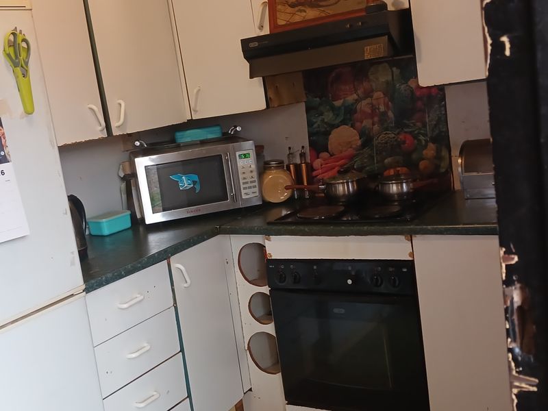 A compact kitchen featuring built-in cabinetry, an electric hob, and an oven. The space shows signs of wear and requires cosmetic updates.