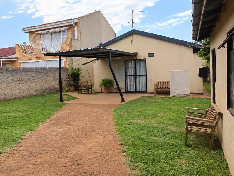 Rear view of the property featuring a covered patio area, a lawn, and a brick boundary wall.