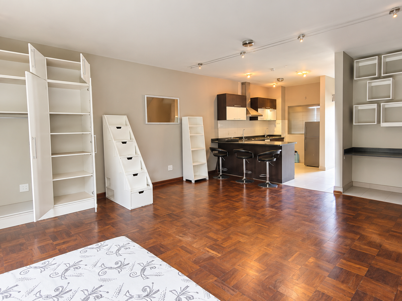 Spacious open-plan living area featuring rich parquet flooring, a modern kitchen with an island, and extensive built-in storage and shelving units.