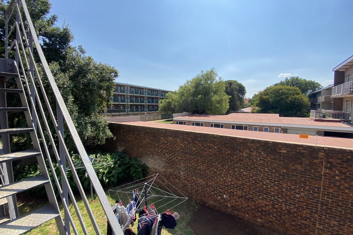 View of the rear exterior area featuring a metal fire escape staircase, a brick boundary wall, and surrounding residential buildings.
