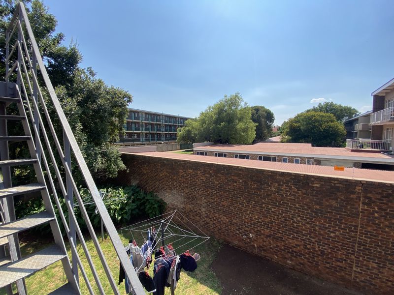 View of the rear exterior area featuring a metal fire escape staircase, a brick boundary wall, and surrounding residential buildings.