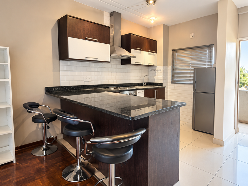 Modern open-plan kitchen featuring dark wood cabinetry, granite countertops, subway tile backsplash, and direct access to a private balcony.