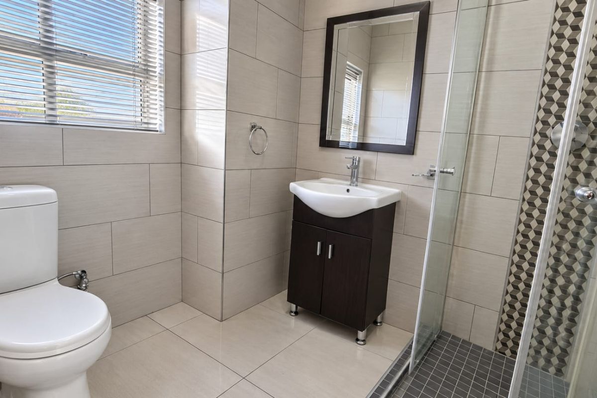 A modern, well-maintained bathroom featuring a vanity unit, toilet, and a glass-enclosed shower with decorative tiled accents.