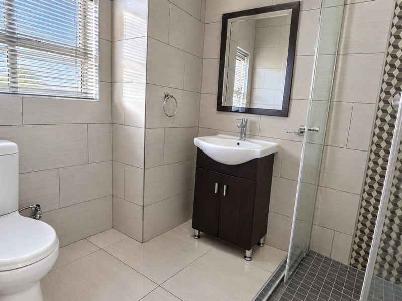 A modern, well-maintained bathroom featuring a vanity unit, toilet, and a glass-enclosed shower with decorative tiled accents.