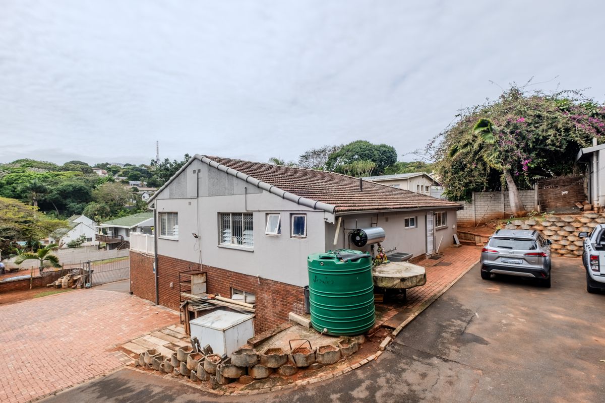Rear exterior view of the property featuring a tiled roof, paved driveway, water storage tank, and solar geyser installation.