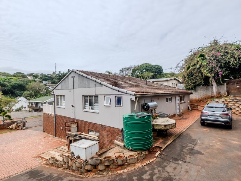 Rear exterior view of the property featuring a tiled roof, paved driveway, water storage tank, and solar geyser installation.