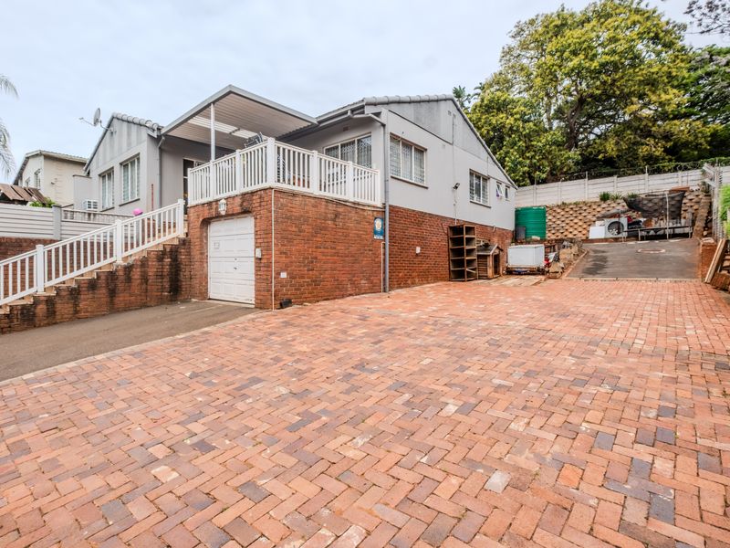 Front exterior view of a house featuring a brick-paved driveway, a single garage, and a raised patio area with white railings.