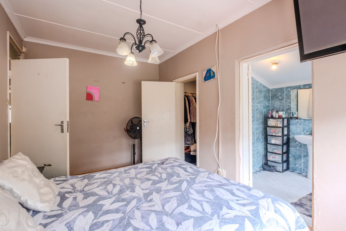 Bedroom featuring an en-suite bathroom, built-in cupboard, and ceiling light fixture. The room requires cosmetic updates to address wall damage and exposed wiring.
