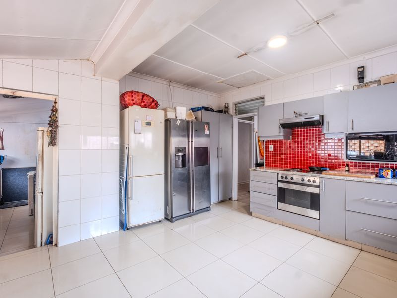 A functional kitchen featuring grey cabinetry, a red tiled splashback, built-in oven, and hob, with tiled flooring throughout.