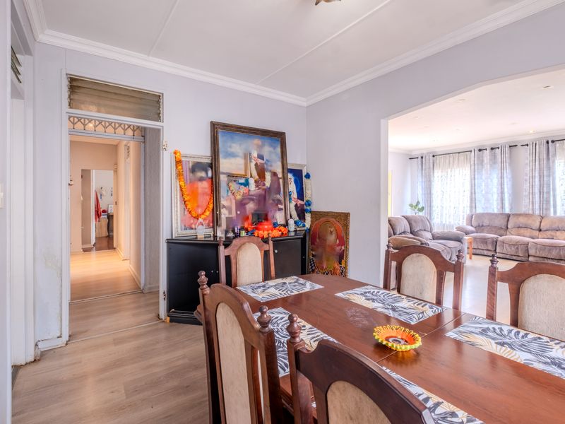 Dining room featuring laminate flooring and crown molding, with an open-plan flow into the adjacent living area and a hallway leading to other rooms.