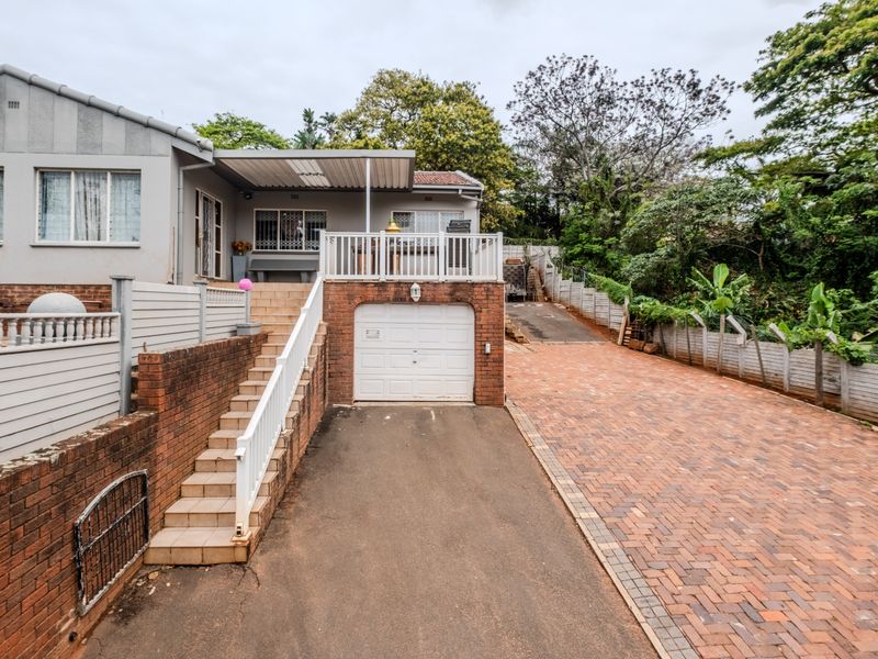 Front exterior view featuring a brick and asphalt driveway, single garage, and a raised covered patio area with stairs leading to the main entrance.