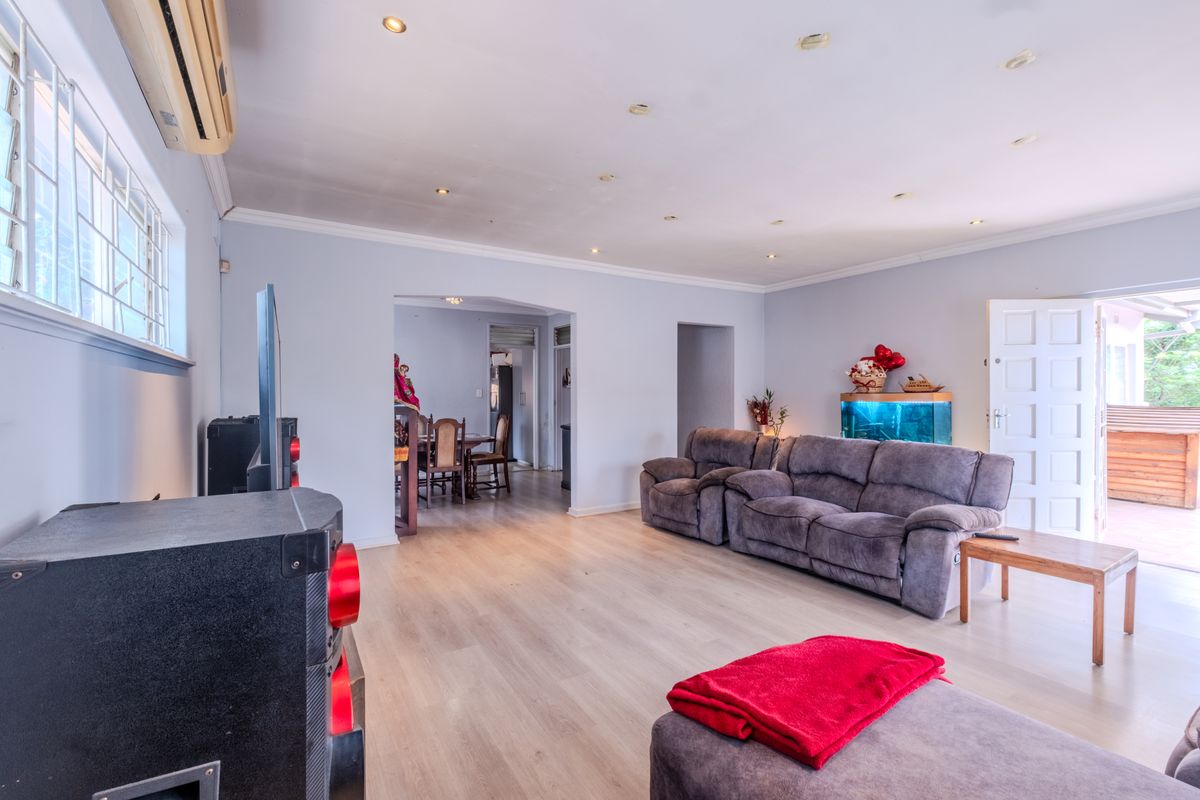 Spacious living room featuring light laminate flooring, recessed downlighting, and a split-system air conditioner, with an open-plan flow to the adjacent dining area.