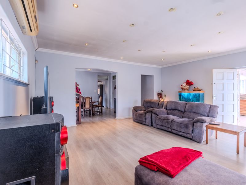 Spacious living room featuring light laminate flooring, recessed downlighting, and a split-system air conditioner, with an open-plan flow to the adjacent dining area.