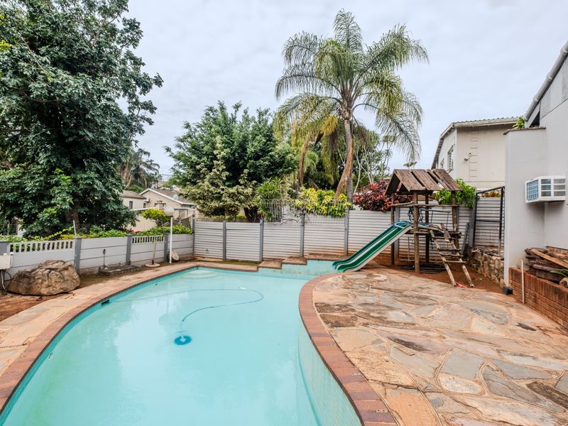 Outdoor pool area featuring a swimming pool with stone paving, boundary wall, and an exterior wall-mounted air conditioning unit.